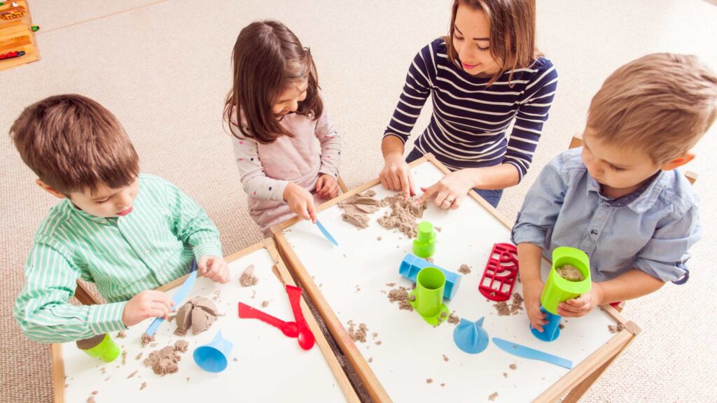 Kinder spielen mit Betreuer am Tisch mit Sand